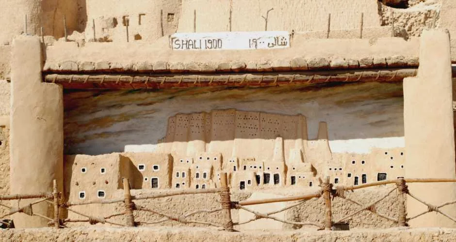 The Shali Fortress ruins glowing amber at sunset with palm groves visible below
